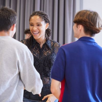A girl wearing a black lacy top has a big smile across her face. She stands facing two boys who have their backs to the camera.